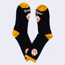 Pair of socks, mostly black with mustard yellow color accents around the calf, toe and ankle of the sock. A small kewpie head is on the ankle with another on the foot with "Giant Robot" written underneath.