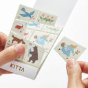 Kitta washi sticker booklet with cartoon-style stamps held by a hand on a white background