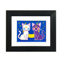 An artwork featuring two stylized cats, one white with blue eyes and a yellow crescent moon on the forehead, and one dark purple with red eyes and a yellow crescent moon on the forehead, seated against a blue background with small yellow stars. In a black frame with a white mat.