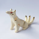 Cream colored sculpture of a sitting 3 tailed fox, with a gold poppy flower design on its back and gold tipped ears, tails and cheeks.
