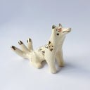 Cream colored sculpture of a sitting 3 tailed fox, with a gold poppy flower design on its back and gold tipped ears, tails and cheeks.