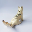 Cream colored sculpture of a sitting 3 tailed fox, with a gold poppy flower design on its back and gold tipped ears, tails and cheeks.