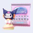 Figurine of Kuromi, dressed in outer space gear and sitting on a yellow planet, in front of her blind bag packaging.