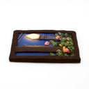 A rectangular sculpture made to look like a miniature painting within a "wooden" frame of a painted night scene, showing a glowing streetlamp, blue sky, green foliage, pink flowers, next to a wooden telephone pole, with wires hanging overhead.