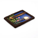 A rectangular sculpture made to look like a miniature painting within a "wooden" frame of a painted night scene, showing a glowing streetlamp, blue sky, green foliage, pink flowers, next to a wooden telephone pole, with wires hanging overhead.