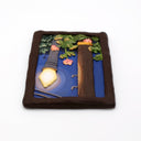 A rectangular sculpture made to look like a miniature painting within a "wooden" frame of a painted night scene, showing a glowing streetlamp, blue sky, green foliage, pink flowers, next to a wooden telephone pole, with wires hanging overhead.
