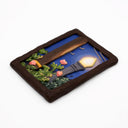 A rectangular sculpture made to look like a miniature painting within a "wooden" frame of a painted night scene, showing a glowing streetlamp, blue sky, green foliage, pink flowers, next to a wooden telephone pole, with wires hanging overhead.