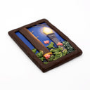A rectangular sculpture made to look like a miniature painting within a "wooden" frame of a painted night scene, showing a glowing streetlamp, blue sky, green foliage, pink flowers, next to a wooden telephone pole, with wires hanging overhead.