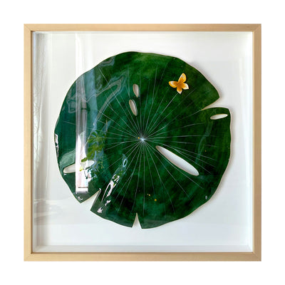Painting on cut out paper of a round, dark green lily pad with thin white lines. A small yellow butterfly is atop the pad. Piece is in a thin, light grain wooden frame.
