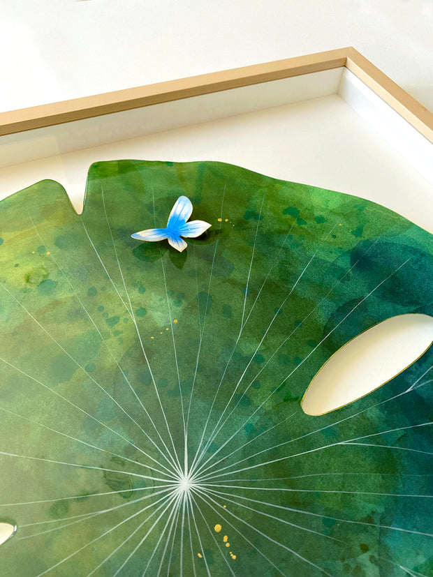 Painting on cut out paper of a round blue and green marble patterned lily pad and thin white lines. A small blue and white butterfly sits atop the pad. Displayed at an angle to show sheen of the resin coating.