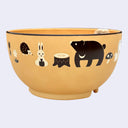 Yellow bowl with cream and brown colored illustrations of forest animals (bear, hedgehog, squirrel, bunny) and forest greenery (mushroom, tree stumps, flowers)