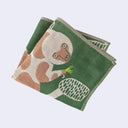 Folded green textile tea towel of a lemur sitting on a tree and holding a small green bug in its hand.