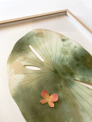 Painted cut out lily pad leaf, greyish green with subtle marbling pattern and thin black stripes. A small blue and yellow butterfly rests atop the leaf. Displayed at an angle to show sheen of resin coating.