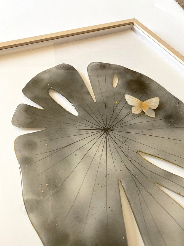 Painted cut out lily pad leaf, dark grey with subtle marbling pattern and thin black stripes. A small white and gold butterfly rests atop the leaf. Displayed at an angle to show sheen from resin coating.