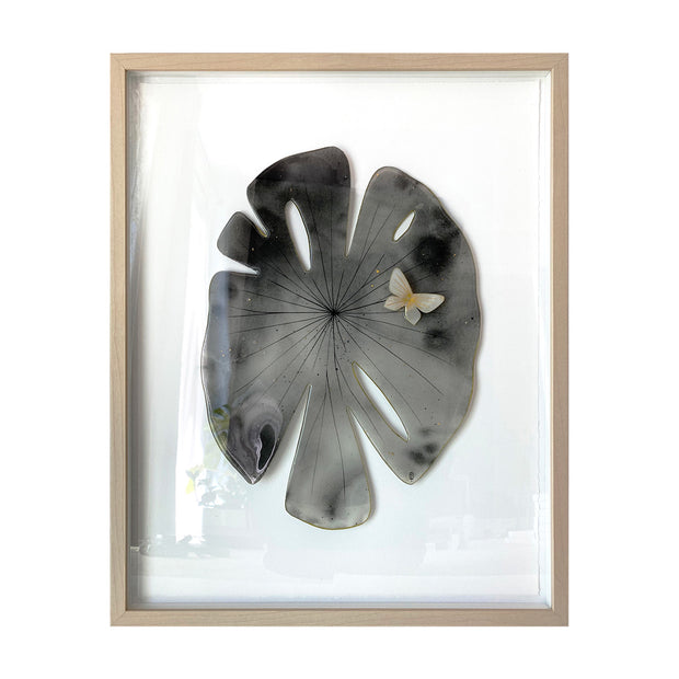 Painted cut out lily pad leaf, dark grey with subtle marbling pattern and thin black stripes. A small white and gold butterfly rests atop the leaf. Piece is framed in thin, light grain wood frame.