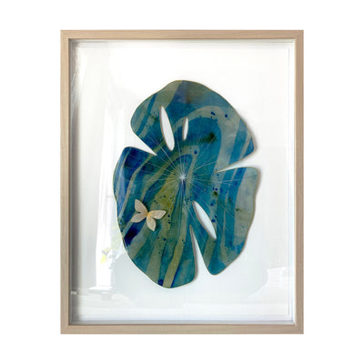 Painted cut out lily pad leaf coated in resin, blue and green with subtle marbling pattern and thin white stripes. A small gold butterfly rests atop the leaf. Piece is in a thin, light grain wood frame.