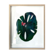 Painted cut out lily pad leaf coated in resin, dark green with subtle marbling pattern and thin white stripes. A small red butterfly rests atop the leaf. Piece is in a thin, light grain wood frame.
