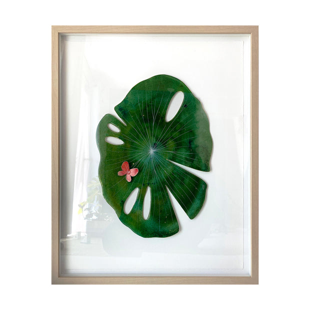 Painted cut out lily pad leaf coated in resin, green with subtle marbling pattern and thin white stripes. A small red butterfly rests atop the leaf. Piece is in a thin, light grain wood frame.