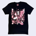 Black t-shirt with a pink graphic design on the front of a girl sitting in a room full of decorative items, plants, art supples and manga. 