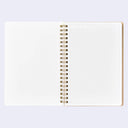 An open spiral-bound notebook with blank white pages on the left and a grid-lined page on the right, bound with gold-tone metal rings, shown on a light lavender background.