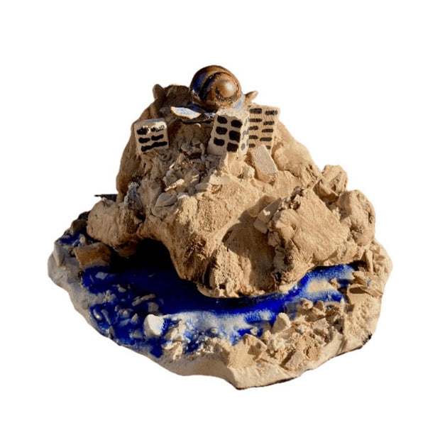 Sculpture of a rock mound, with a few city buildings coming out the top and a large snail atop them. A blue river runs along the center of the rocks.