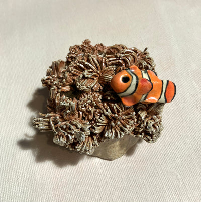 Ceramic sculpture of a sea anemone, brown with many tendrils. Atop of it rest a small clownfish.