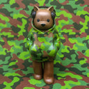 A stylized bear figurine wearing a green camouflage hoodie and black headphones, standing against a matching camouflage patterned background.