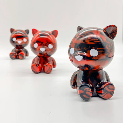 3 small sofubi bears with large heads, red with black marbling. They sit on the floor with large eyes and a nose and no other defining facial features.