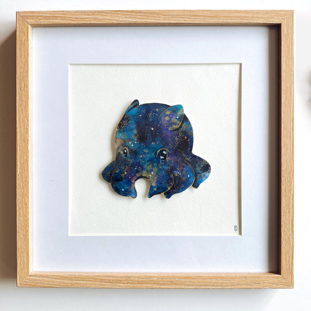 Small galaxy colored dumbo octopus, made out of cut paper and mounted on a cream colored background. Piece is framed within a thin wooden frame.