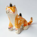 Glossy ceramic sculpture of an orange tiger with a carved pattern of poppy flowers on its body, with various stripes. Sitting on its back and head are small black magpie birds.