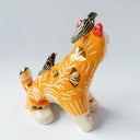 Glossy ceramic sculpture of an orange tiger with a carved pattern of poppy flowers on its body, with various stripes. Sitting on its back and head are small black magpie birds.