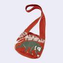 Dark reddish-orange shoulder bag with a graphic in green and white of a malay bear, under some leaves.