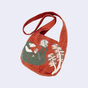 Dark reddish-orange shoulder bag with a graphic in green and white of a malay bear, under some leaves.