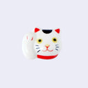 3D ceramic brooch/pin of a maneki cat's head with one paw raised upward. It has a smile, yellow eyes and a red collar.