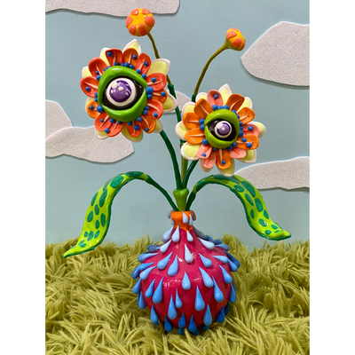 Very colorful semi psychedelic inspired sculpture of a hot pink plant bot with blue water droplets running out of it. A plant with 2 flower buds has eyes for their centers, coming out of the pot.