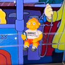 Figure of Martin Prince from The Simpsons, wearing a shirt that says "Wang Computers", sitting and holding a book at his side. 