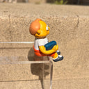 Figure of Martin Prince from The Simpsons, wearing a shirt that says "Wang Computers", sitting and holding a book at his side. 