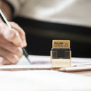 Square eraser in a plastic casing, with a black holder on the bottom and a brown clear plastic cap. It is being displayed on a desk.