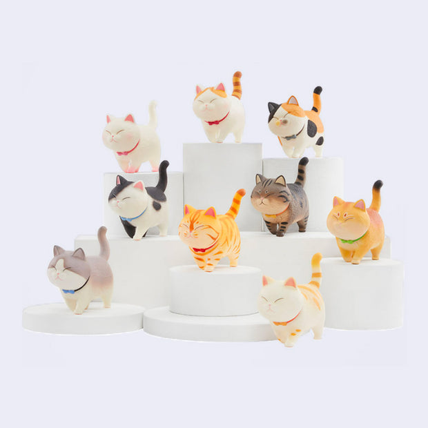 9 different cat figurines, all walking with their tails straight up and happy closed eye expressions. Their color ways vary.