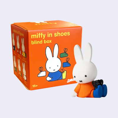 Figure of Miffy, sitting in an orange shirt with blue shoes. She sits in front of an orange blind box that reads "miffy in shoes blind box"
