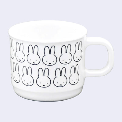 Small white handle mug with a repeating design of Miffy's face, with her small eyes and x shaped mouth. 