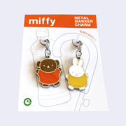 2 die cut metal charms, one of Miffy in a yellow dress and one of Miffy's friend Boris the bear, in her orange dress. Each are attached to their own clasp on a white backing card. Shown at an angle to display sheen.