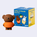 Toy figure of a bear in an orange shirt next to a 'miffy & friends' blind box on a light gray background