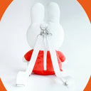 Miffy plush, wearing an orange dress with a white collar. She has straps that make it a backpack. Zipper opening on the back.