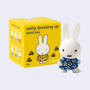 Miffy figurine in a blue dress next to its packaging box on a white background