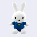 Plush Miffy doll, sitting with a blue shirt dress and a small embroidered yellow button.
