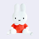 Miffy plush, wearing an orange dress with a white collar. She has straps that make it a backpack.