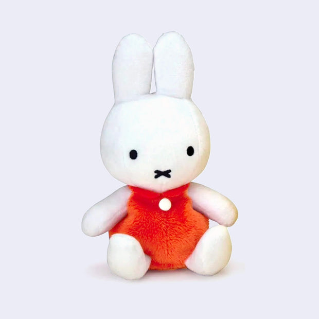 Bright white Miffy plush, sitting down and wearing a short sleeve orange dress with a single white button.