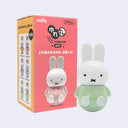 Figurine of Miffy wearing a pastel green shirt with a round, ball-like bottom, which allows the figure to wobble around without toppling over. Sitting next to its product packaging.