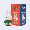 Figurine of Miffy wearing a green shirt with a round, ball-like bottom, which allows the figure to wobble around without toppling over. Sitting next to its product packaging.